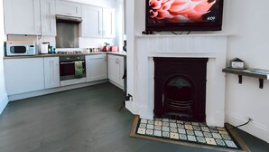 A modern kitchen with white cabinets, a microwave, a stove, and a flat-screen TV mounted above a fireplace. - The Twickenham Apartment Near Strawberry Hill (Twickenham)