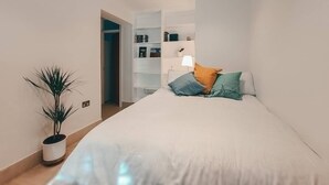 Ein modernes Schlafzimmer mit einem Bett, einer Topfpflanze und einer Regalwand mit Büchern und Dekoration.