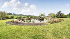 Ein angelegter Garten mit einem zentralen Teich, einer Bank und verschiedenen Pflanzen.