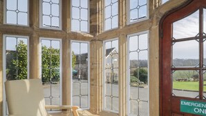 A room with a large window, a wooden bench, and an emergency exit sign. - Harcombe House Rooms Accessible Ground Floor Twin (Newton Abbot)