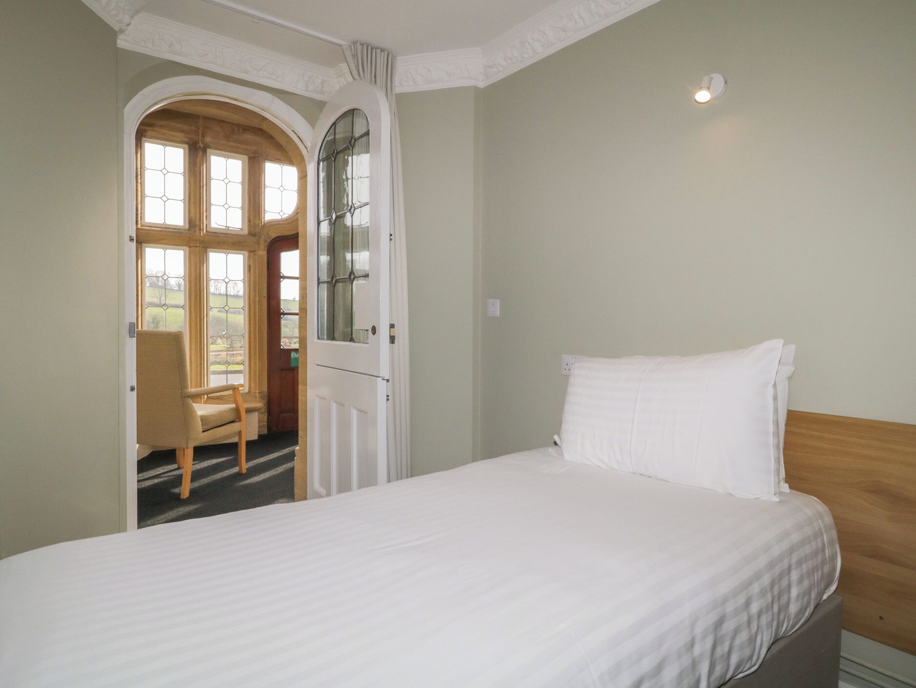 Een slaapkamer met een bed, een stoel en een deur die leidt naar een balkon.