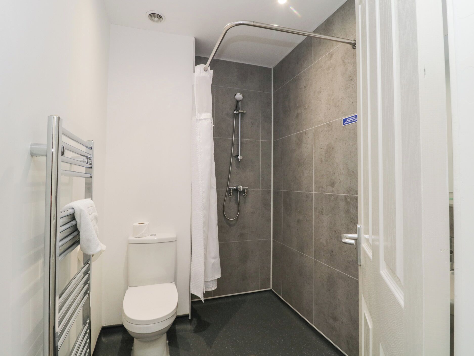 Egy modern fürőszoba, zuhanyzóval, WC-vel és törölközőtartóval.
