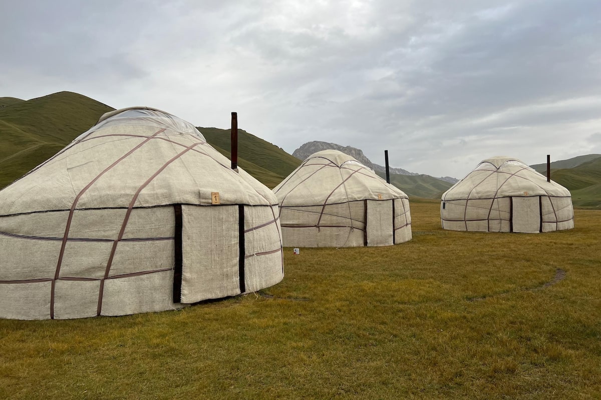 Three yurts in a grassy field with mountains in the background.