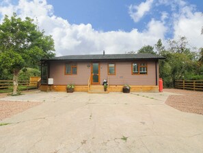 A small wooden building with a brown door and windows, surrounded by a gravel driveway and wooden fences. - Dunromin (Montgomery)