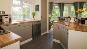 A modern kitchen with a dishwasher, a coffee maker, and a toaster. There is a window with curtains and a view of greenery outside.