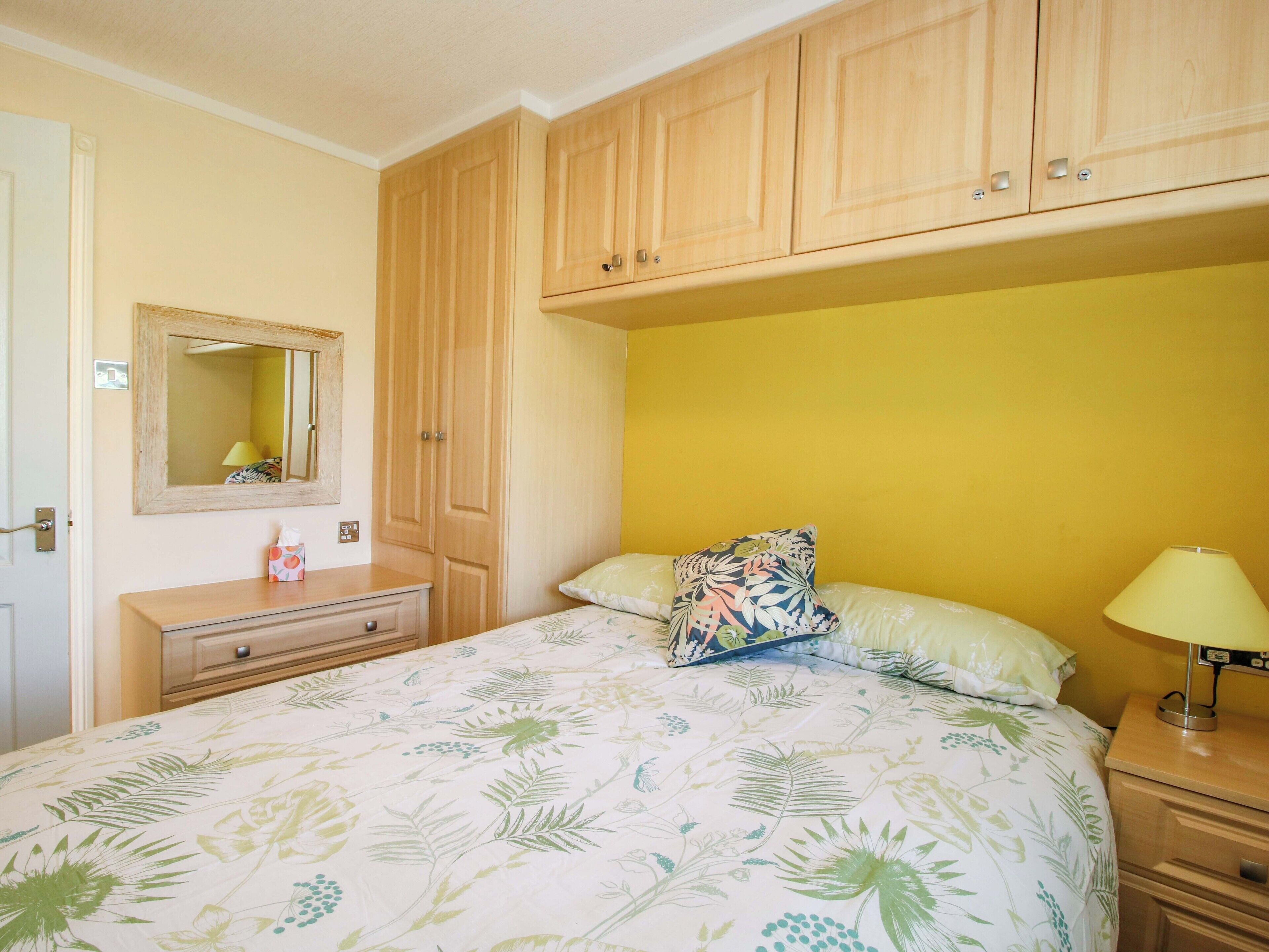 A bedroom with a bed, a nightstand, a dresser, a mirror, and wooden cabinets.