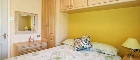 A bedroom with a bed, a nightstand, a dresser, a mirror, and wooden cabinets.