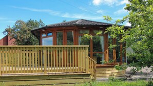 A wooden gazebo with a tiled roof, surrounded by a wooden deck and lush greenery.