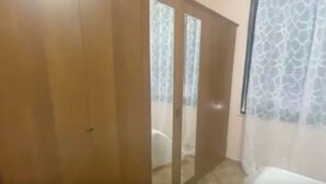 A room with a wooden wardrobe, a bed, and a window with patterned curtains. - Sea View Apartment in Durres Albania (Durrës)