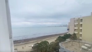 A view of a beach from a window overlooking a building with a flat roof and a balcony. - Sea View Apartment in Durres Albania (Durrës)