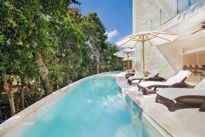 A poolside area with lounge chairs and umbrellas, surrounded by lush greenery.