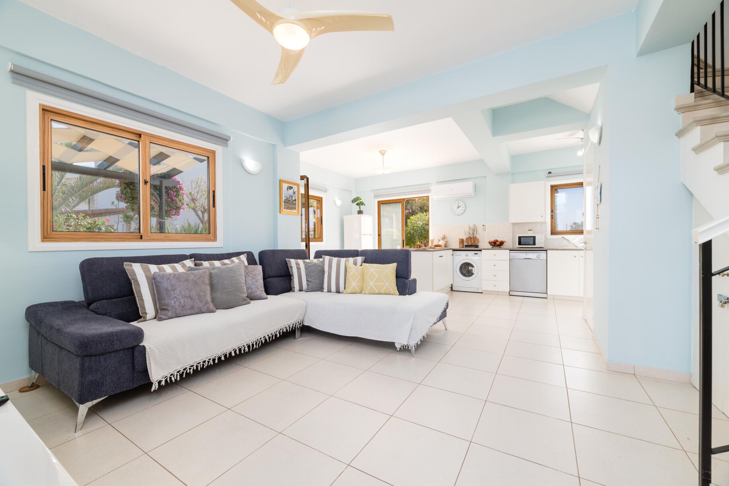 A modern living room with a sectional sofa, a ceiling fan, and a view to the kitchen.