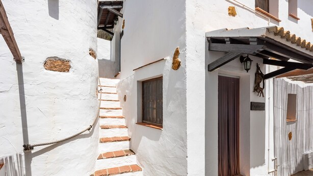 Un bâtiment étroit aux murs blancs, doté d’un escalier en pierre, d’une porte en bois et d’une petite fenêtre.