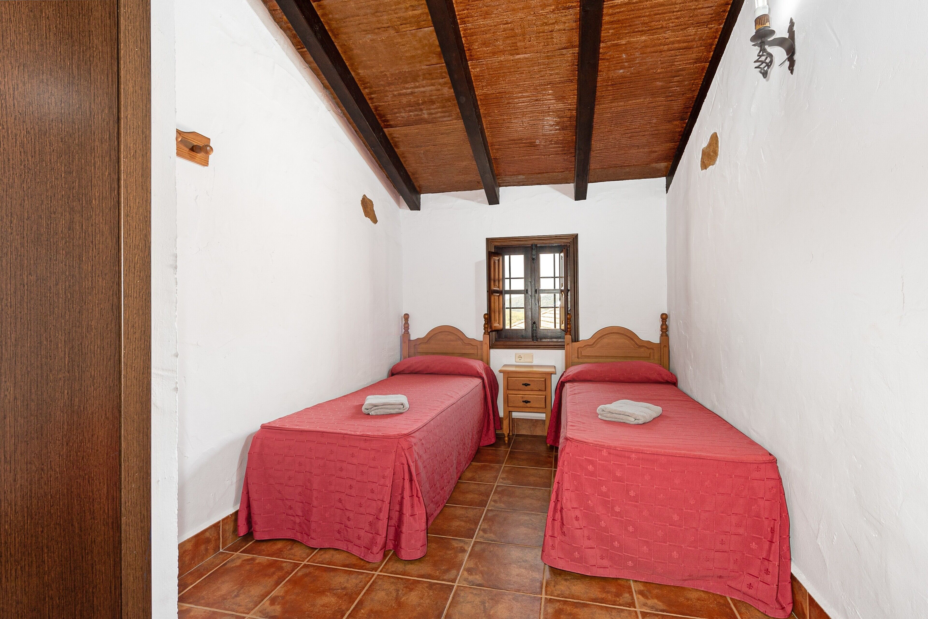 A room with two beds, a wooden ceiling, a window, and a small table.