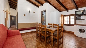 Un coin repas avec une table et des chaises en bois, un canapé rouge et une cuisine équipée d’un lave-linge.