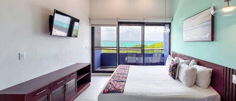 Une chambre avec un lit, une télévision, un ventilateur de plafond et un balcon offrant une vue sur l’océan.