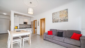 A modern living room with a grey sofa, a dining table with chairs, and a kitchen in the background. - Apartment 'Solmonte' with Shared Pool, Wi-Fi and Air Conditioning (Portimão)