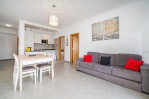 Una sala de estar moderna con un sofá gris, una mesa de comedor con sillas y una cocina al fondo.