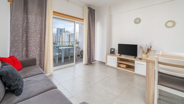 A modern living room with a sofa, TV, and a view of the city. - Apartment 'Solmonte' with Shared Pool, Wi-Fi and Air Conditioning (Portimão)