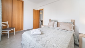 A bedroom with a large wardrobe, a bed with patterned bedding, and a chair. - Apartment 'Solmonte' with Shared Pool, Wi-Fi and Air Conditioning (Portimão)