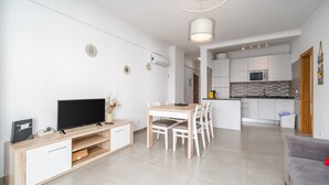 A modern living room with a TV, wooden entertainment unit, dining table, and chairs. - Apartment 'Solmonte' with Shared Pool, Wi-Fi and Air Conditioning (Portimão)