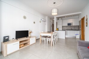 A modern living room with a TV, wooden entertainment unit, dining table, and chairs.