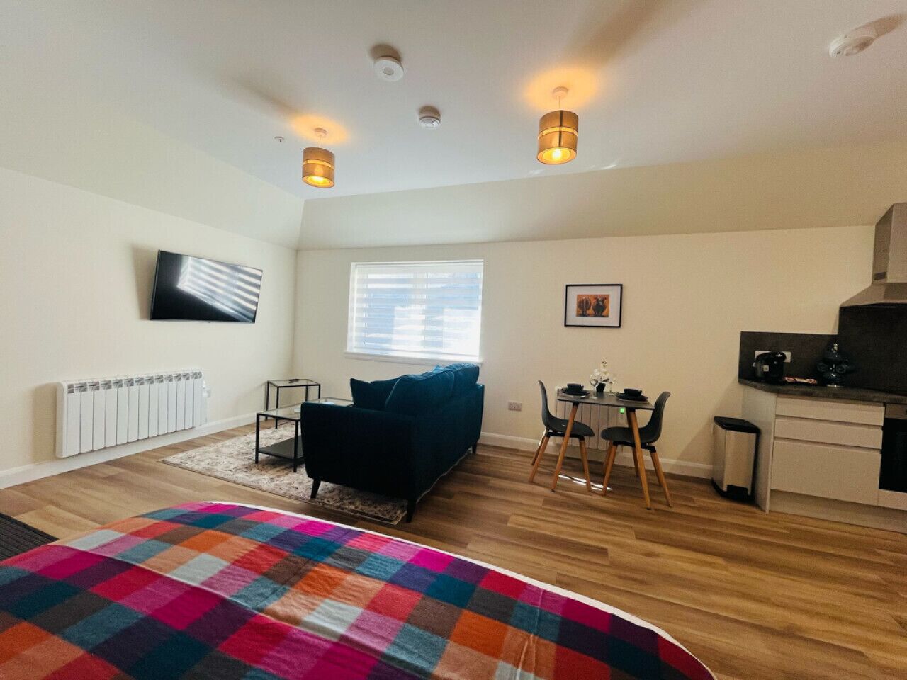 A compact living space with a sofa, a dining table, a kitchen area, and a TV mounted on the wall.