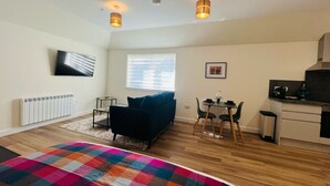 A compact living space with a sofa, a dining table, a kitchen area, and a TV mounted on the wall. - Viewforth Studio No.4 (Fort William)