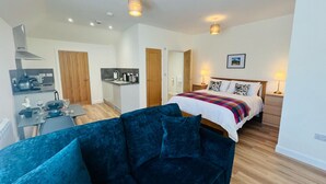 A modern room with a blue sofa, a bed with a colorful blanket, a kitchen area, and a dining table. - Viewforth Studio No.4 (Fort William)
