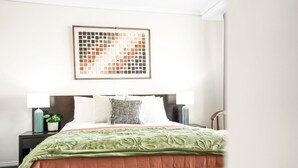 Una camera d'albergo con un letto, due comodini, un'opera d'arte appesa al muro e un tavolino da notte con una lampada e una pianta.