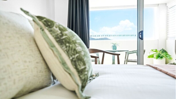 Una camera d'albergo con un letto, vista sul cielo e un balcone con tavolo e sedie.
