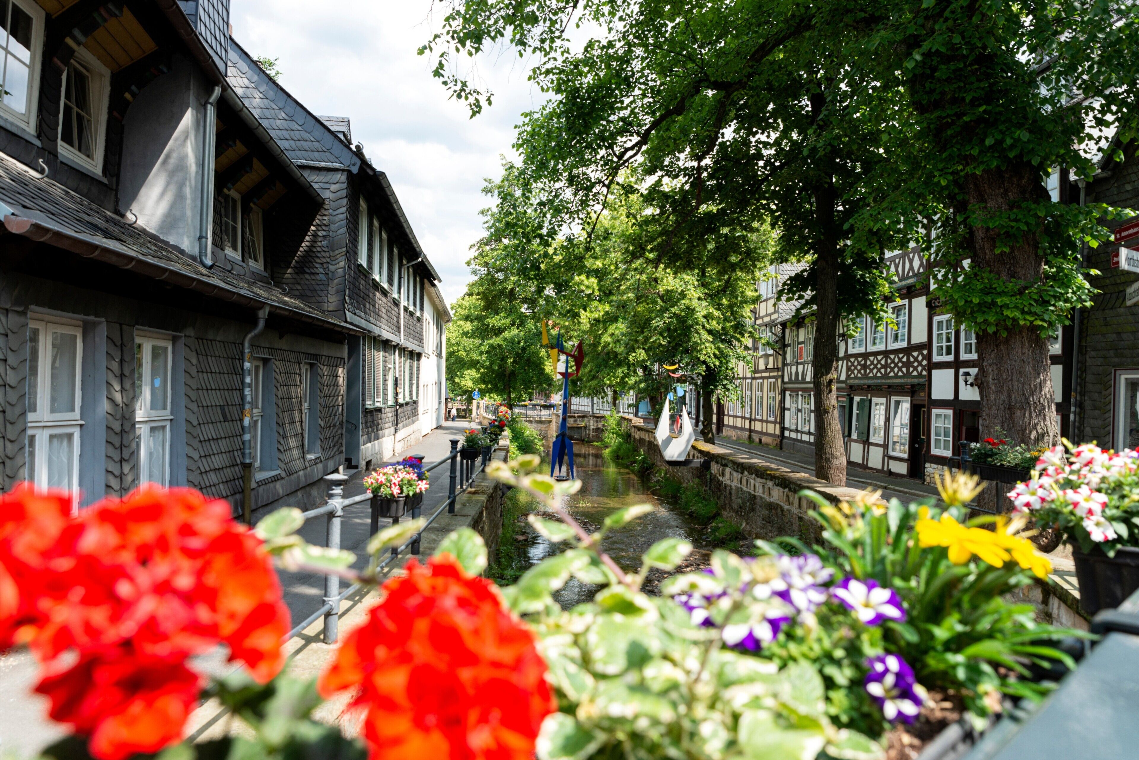 Une rue étroite bordée de bâtiments traditionnels à colombages, un canal et des trottoirs ornés de fleurs.
