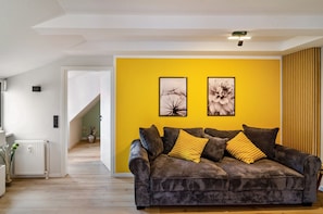 A living room with a sofa, two framed pictures, a radiator, and a wooden floor. - Apartment 'Domschatz' with Wi-Fi and Air Conditioning (Goslar)