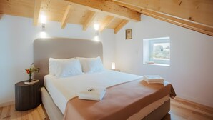 Ein Schlafzimmer mit Bett, Nachttischlampen, einem Fenster und einer Holzbalkendecke.