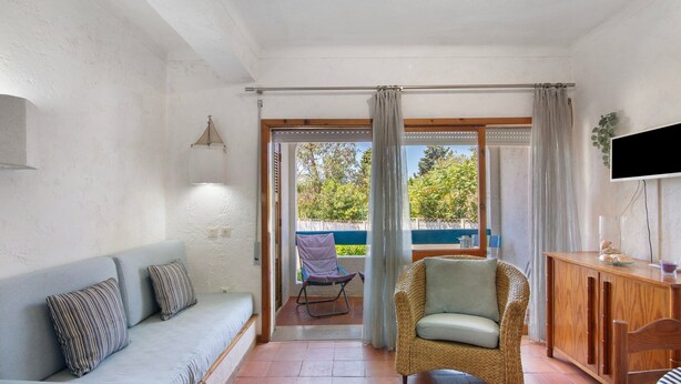 A room with a sofa, a wicker chair, a wooden cabinet, and a television.