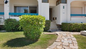 A building with a stone pathway leading to a set of stairs, surrounded by greenery and a clear sky.
