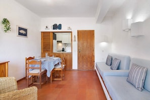 A room with a dining table, chairs, a sofa, a wooden door, and a small kitchen area.