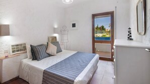 A bedroom with a bed, bedside table, lamp, and a view of a balcony.