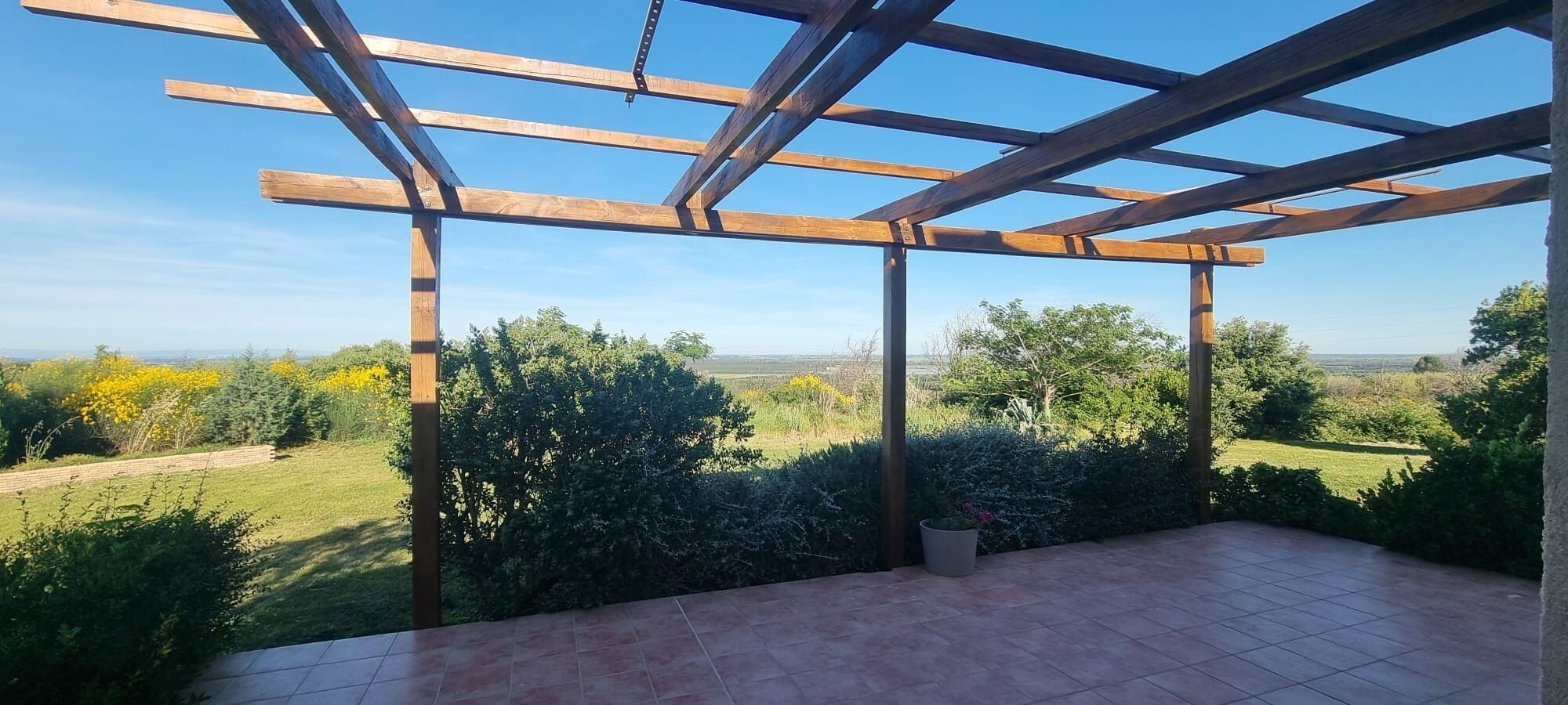 A covered patio with a view of a grassy landscape and trees.