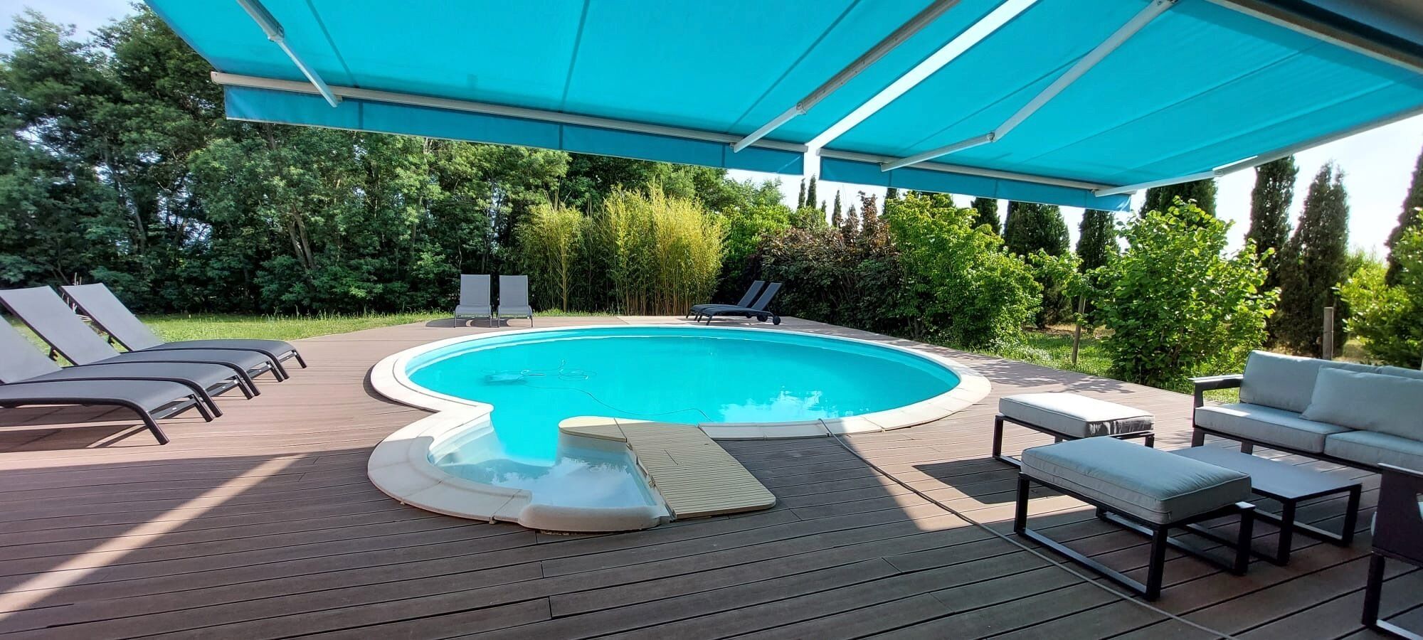 A swimming pool with a deck, lounge chairs, and a covered seating area.