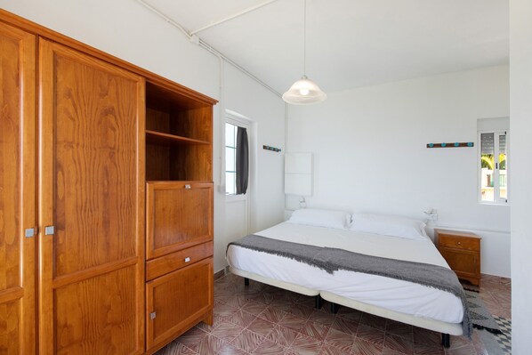 A bedroom with a bed, wooden wardrobe, bedside table, and a hanging light fixture.
