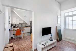 Un espacio habitable compacto con cocina, comedor y televisor sobre un soporte blanco.