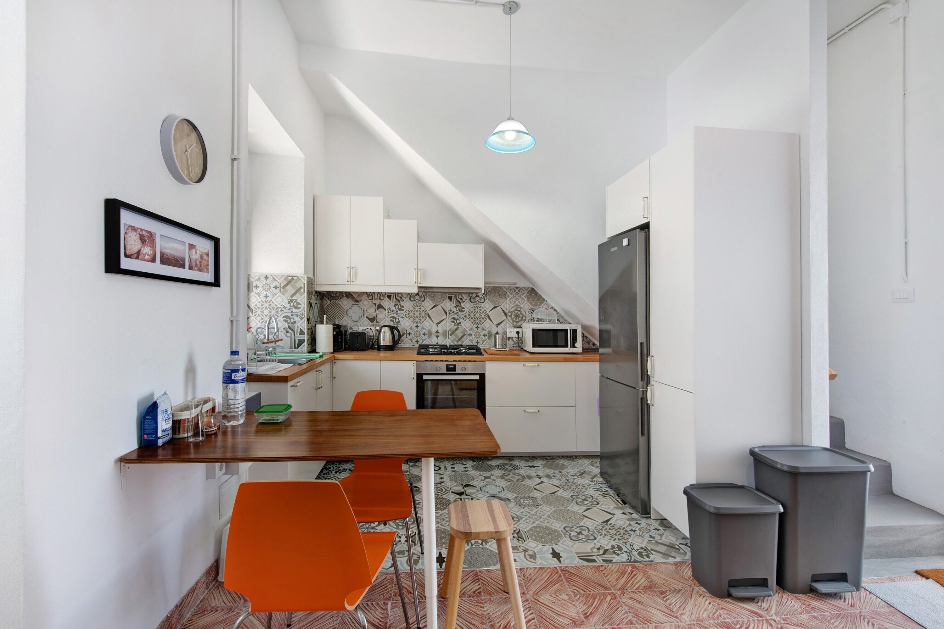 Een moderne keuken met een houten tafel, oranje stoelen, een magnetron en een koelkast.