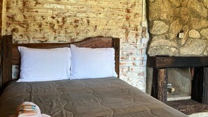Un lit avec des oreillers blancs, une tête de lit en bois et un mur en pierre derrière.