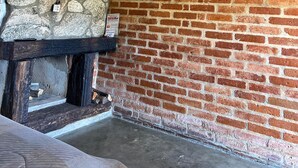 Une pièce au décor rustique, avec une cheminée en pierre, un mur en briques et un téléviseur fixé au mur.