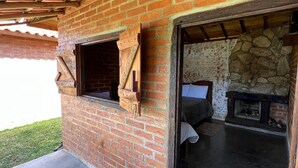 Un bâtiment rustique en briques, avec un plafond en bois, une cheminée en pierre et un lit visible à l’intérieur.