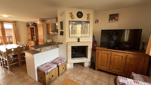 Uma área de estar aconchegante com lareira, armários de madeira, uma TV e uma mesa de jantar.