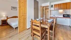 A compact room with a wooden bed, a dining table set for four, a kitchenette with a microwave, and a wooden wardrobe. - 40m from ski slopes, 1st floor, fitness, swimming pool, sauna, balcony, tv, ski locker, 30-38m² (Les Orres)