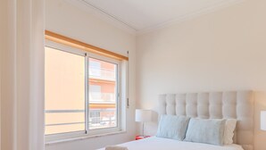 A bedroom with a large window, a bed with a tufted headboard, two bedside lamps, and a view of a building outside.