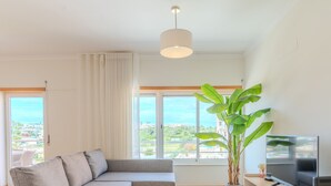 A modern living room with a sofa, a large window, a plant, and a television.